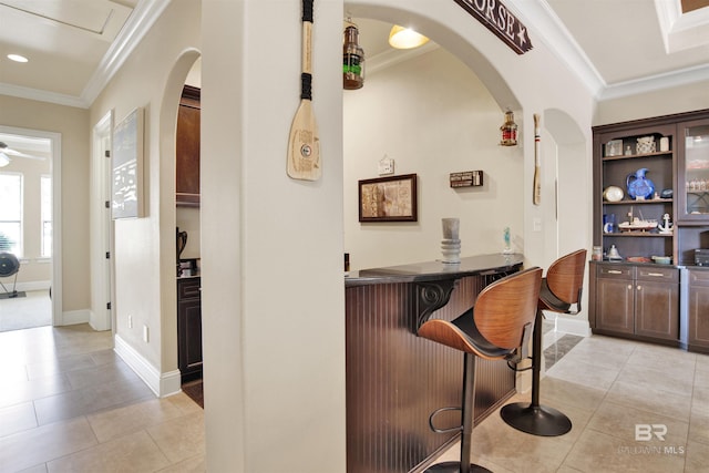 bar featuring crown molding, arched walkways, baseboards, and light tile patterned floors