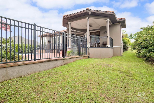 exterior space featuring a tiled roof, ceiling fan, a lawn, fence, and stucco siding