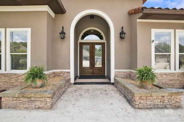 view of exterior entry featuring french doors, stucco siding, and stone siding