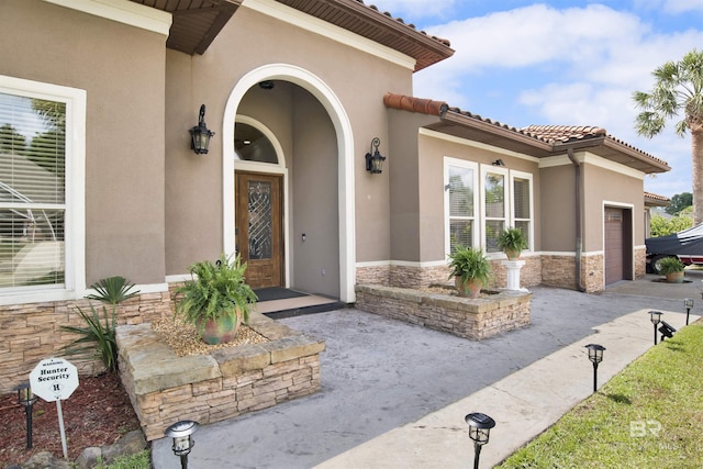 doorway to property featuring a garage, stucco siding, and stone siding
