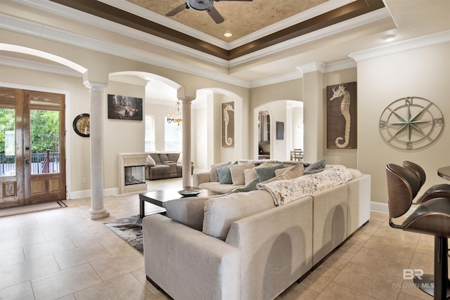 living room with ceiling fan, decorative columns, arched walkways, light tile patterned floors, and a tray ceiling