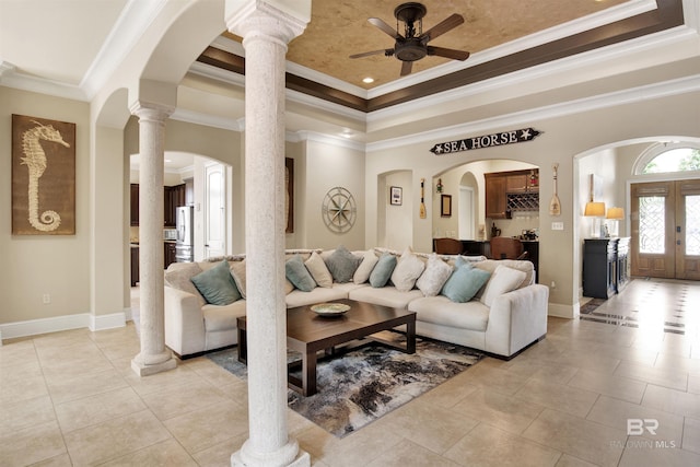 living room featuring ornamental molding, light tile patterned flooring, baseboards, ceiling fan, and a tray ceiling