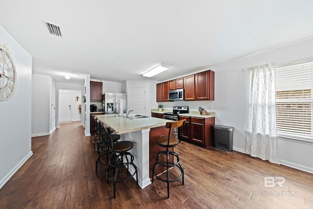 kitchen with a breakfast bar, dark wood-type flooring, an island with sink, stainless steel appliances, and sink