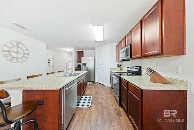 kitchen featuring stainless steel appliances, wood-type flooring, a breakfast bar, and sink