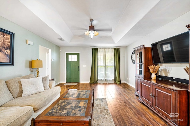 living room featuring a raised ceiling, dark wood-type flooring, and ceiling fan