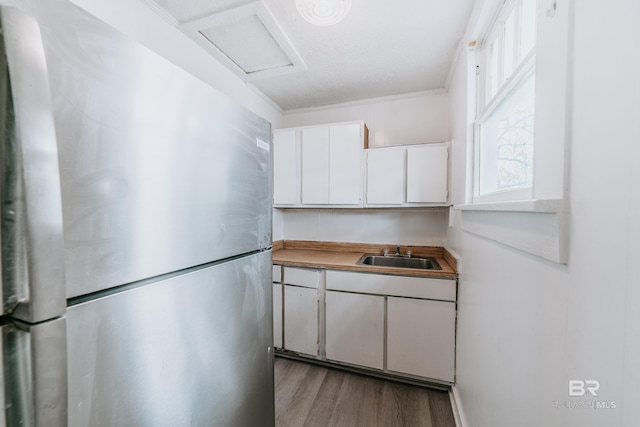 kitchen featuring sink, white cabinetry, light hardwood / wood-style flooring, ornamental molding, and stainless steel fridge