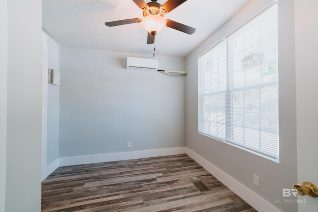 spare room featuring a wall unit AC, ceiling fan, a wealth of natural light, and dark wood-type flooring