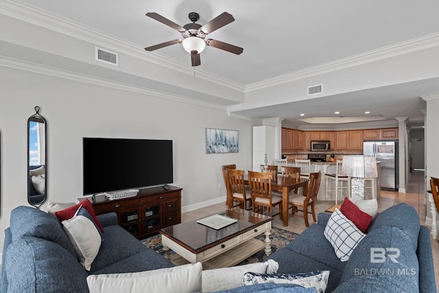 living area with a tray ceiling, visible vents, crown molding, and decorative columns