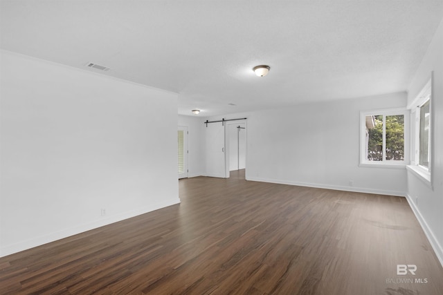 spare room featuring visible vents, a barn door, dark wood finished floors, and baseboards