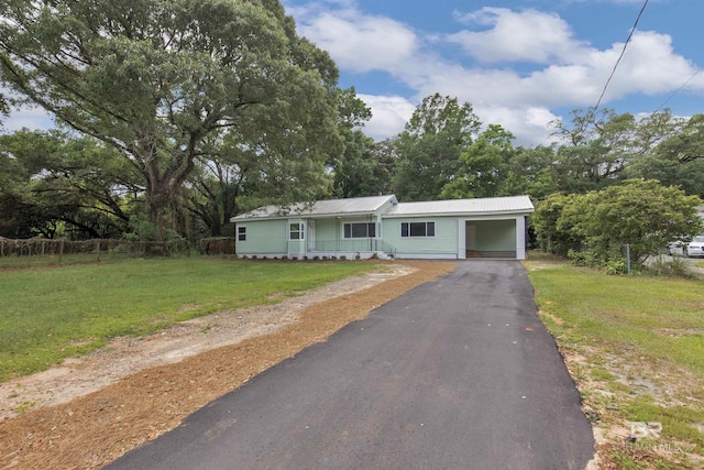 view of front facade with aphalt driveway, metal roof, a carport, fence, and a front lawn