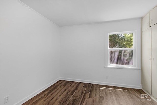 empty room featuring crown molding, baseboards, and wood finished floors