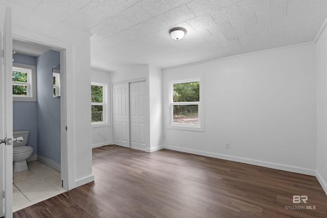 unfurnished bedroom featuring a closet, connected bathroom, dark wood finished floors, and baseboards