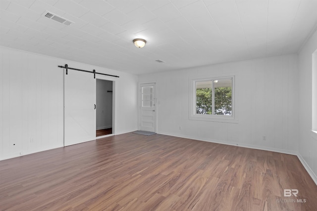 empty room with visible vents, a barn door, and wood finished floors