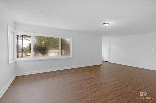 spare room featuring baseboards and dark wood-style floors