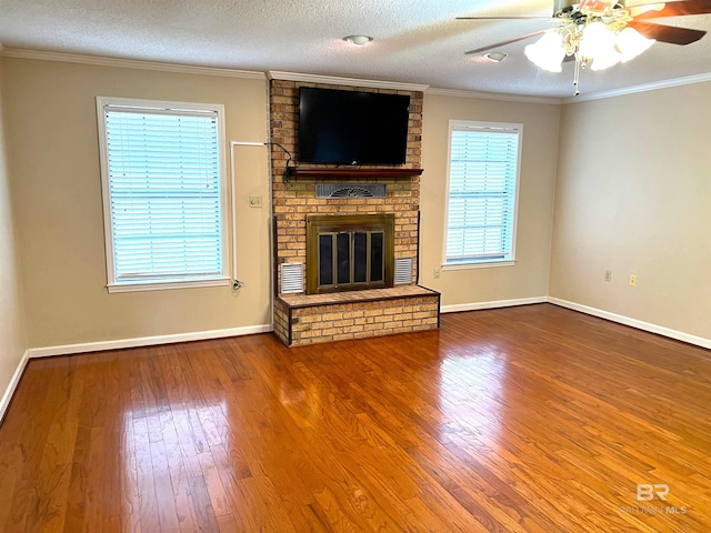 unfurnished living room with a textured ceiling, hardwood / wood-style floors, ceiling fan, a brick fireplace, and crown molding