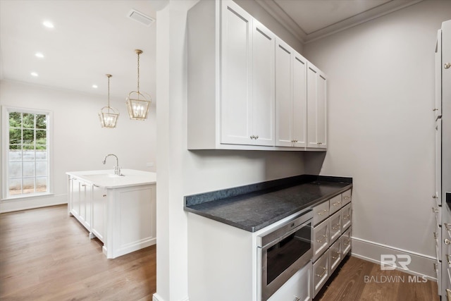 kitchen featuring sink, white cabinetry, crown molding, hanging light fixtures, and light wood-type flooring