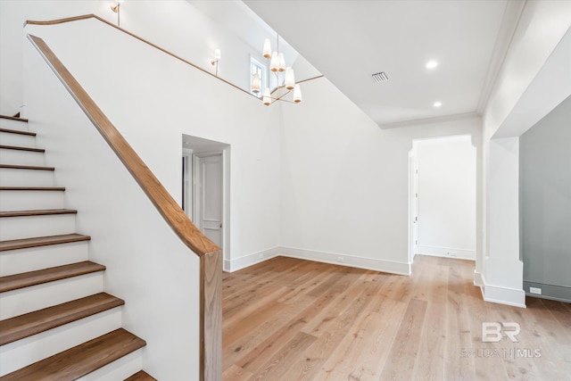 stairway featuring crown molding, wood-type flooring, and an inviting chandelier