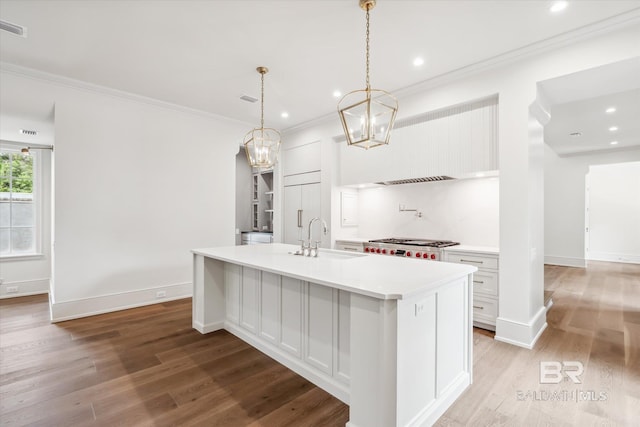 kitchen featuring pendant lighting, sink, crown molding, white cabinetry, and an island with sink