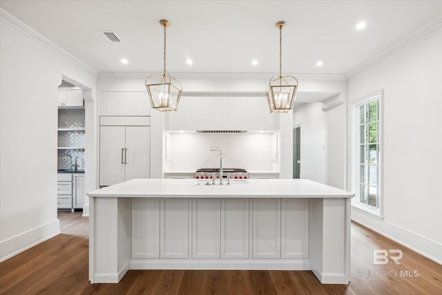 kitchen featuring hardwood / wood-style floors, decorative backsplash, paneled fridge, an island with sink, and decorative light fixtures