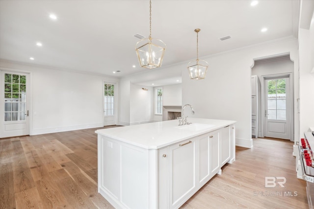 kitchen with sink, decorative light fixtures, a center island with sink, light wood-type flooring, and white cabinets