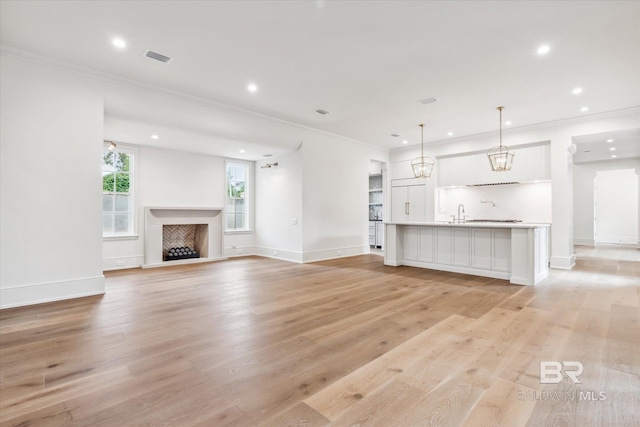 unfurnished living room with crown molding, sink, and light hardwood / wood-style floors