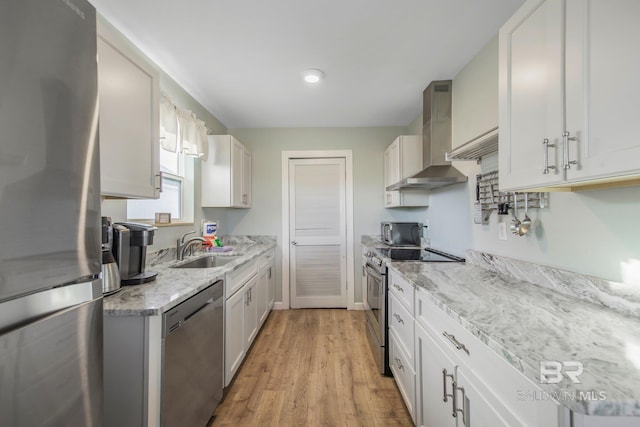 kitchen featuring stainless steel appliances, sink, wall chimney range hood, white cabinets, and light hardwood / wood-style floors