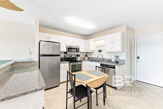 kitchen with a sink, light tile patterned floors, stainless steel appliances, and white cabinetry