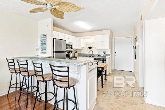 kitchen featuring white cabinets, a breakfast bar, a sink, stainless steel appliances, and a peninsula