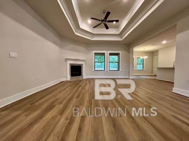 unfurnished living room featuring hardwood / wood-style floors, ceiling fan with notable chandelier, a raised ceiling, and crown molding