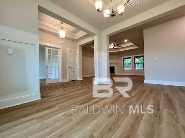 unfurnished living room with a tray ceiling, wood-type flooring, and ceiling fan with notable chandelier