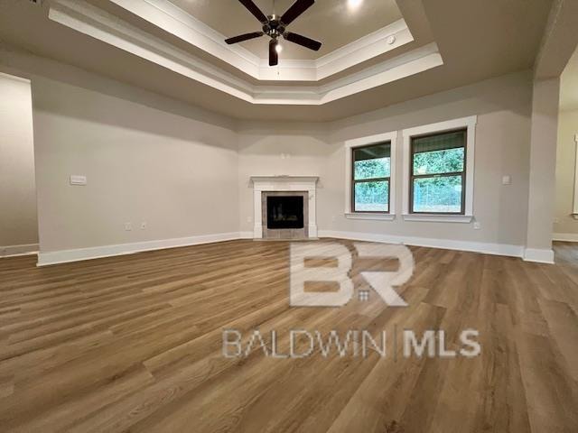 unfurnished living room with ornamental molding, hardwood / wood-style floors, ceiling fan, and a raised ceiling