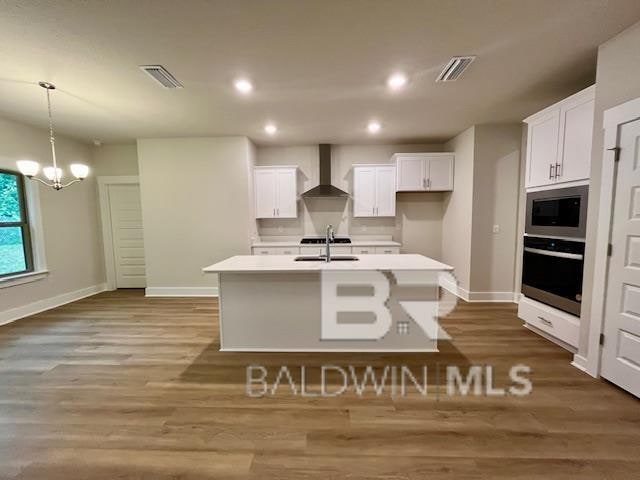 kitchen featuring white cabinets, wall chimney exhaust hood, a kitchen island with sink, and appliances with stainless steel finishes