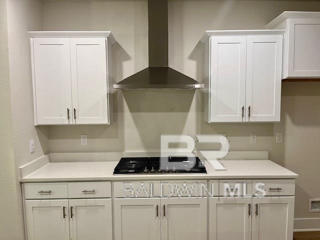 kitchen featuring white cabinets, black gas cooktop, and wall chimney range hood