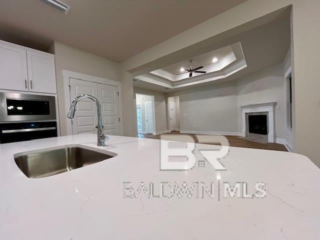 kitchen featuring sink, light stone counters, ornamental molding, ceiling fan, and a tray ceiling