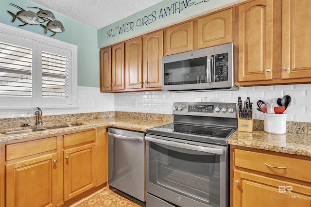 kitchen featuring light stone countertops, a sink, stainless steel appliances, a textured ceiling, and tasteful backsplash