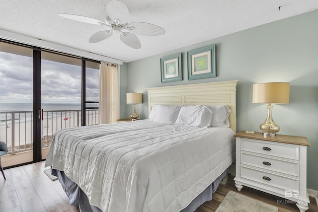 bedroom with access to exterior, ceiling fan, expansive windows, wood finished floors, and a textured ceiling