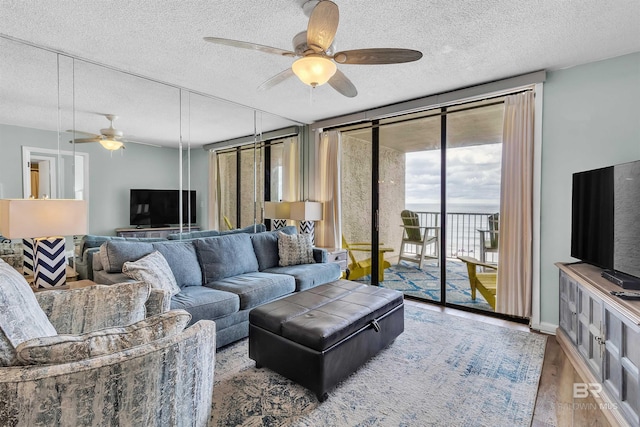 living room featuring a textured ceiling, wood finished floors, baseboards, ceiling fan, and expansive windows