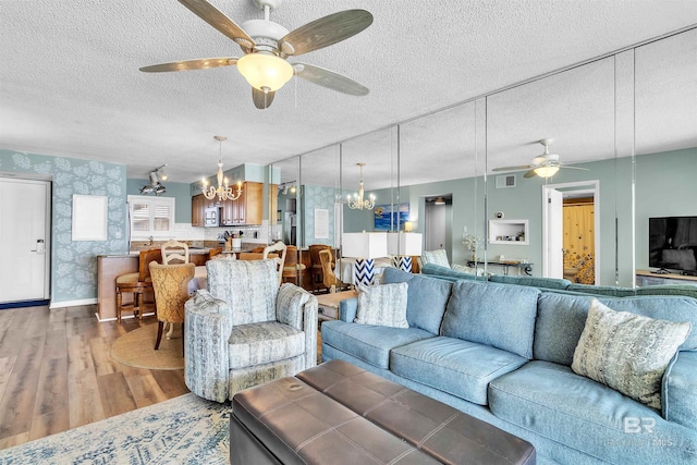 living area with light wood finished floors, visible vents, a textured ceiling, and wallpapered walls