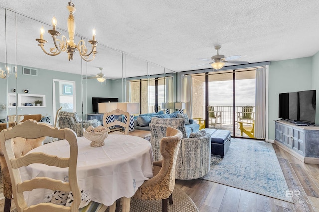 dining area with visible vents, ceiling fan with notable chandelier, a wall of windows, and wood finished floors