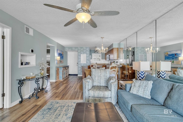 living room featuring wood finished floors, baseboards, visible vents, a textured ceiling, and ceiling fan with notable chandelier