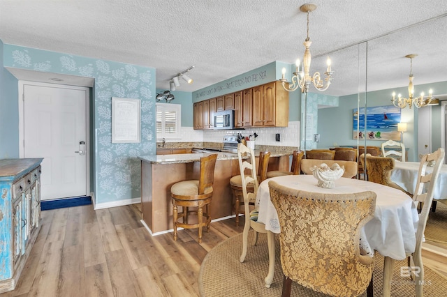 kitchen featuring wallpapered walls, an inviting chandelier, light wood-style flooring, stainless steel appliances, and a textured ceiling