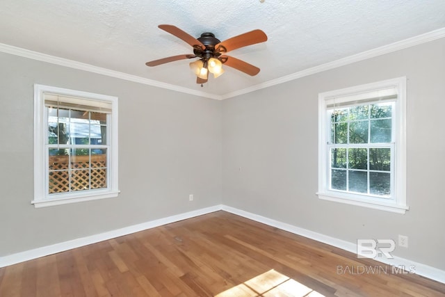 spare room with a textured ceiling, ornamental molding, wood finished floors, and baseboards