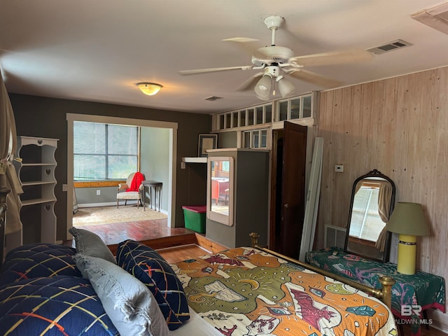 bedroom with hardwood / wood-style floors, ceiling fan, and wood walls