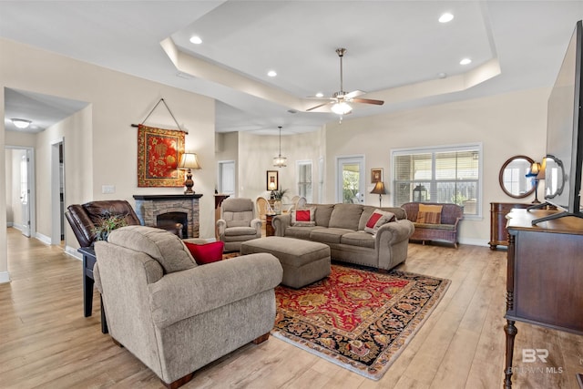 living room featuring ceiling fan, a fireplace, a tray ceiling, and light hardwood / wood-style flooring