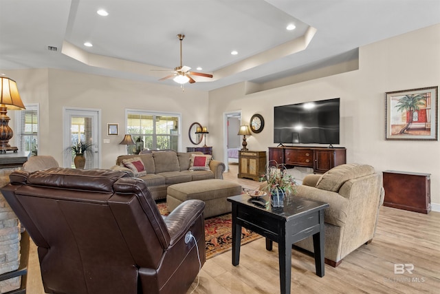 living room with light hardwood / wood-style floors, a raised ceiling, and ceiling fan