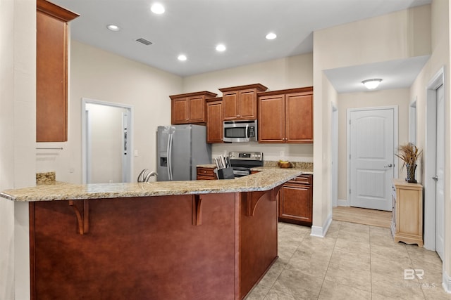 kitchen with stainless steel appliances, light stone countertops, a kitchen breakfast bar, and kitchen peninsula