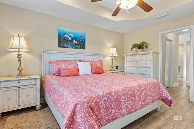 bedroom with a raised ceiling, ceiling fan, and light hardwood / wood-style floors