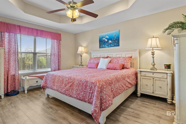 bedroom featuring ceiling fan, a raised ceiling, and light hardwood / wood-style floors