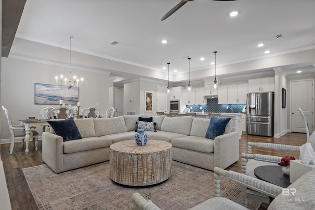 living room with dark wood-type flooring, ornamental molding, and ceiling fan with notable chandelier