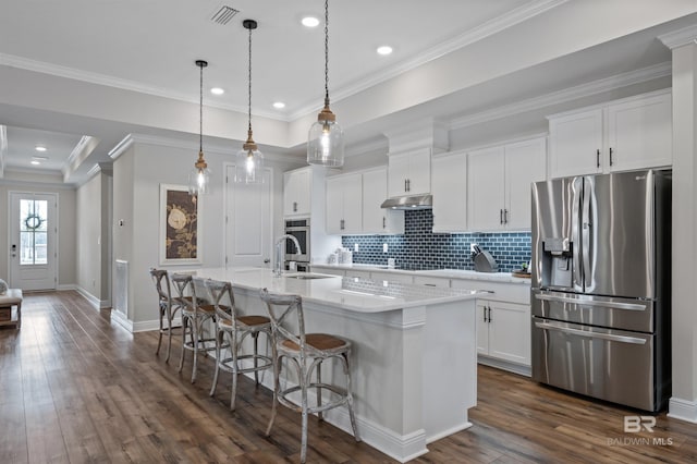 kitchen featuring sink, appliances with stainless steel finishes, a kitchen island with sink, hanging light fixtures, and white cabinets